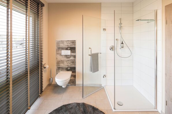 Modernes Badezimmer im FingerHaus NEO Musterhaus Günzburg mit bodengleicher Dusche, Glastrennwand und WC.