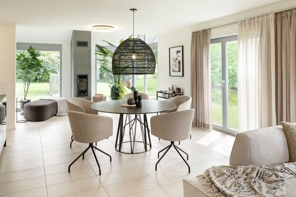Heller Essbereich im frei geplanten FingerHaus Musterhaus Marburg mit rundem Tisch, modernen Polsterstühlen und großer Fensterfront mit Zugang zum Garten.