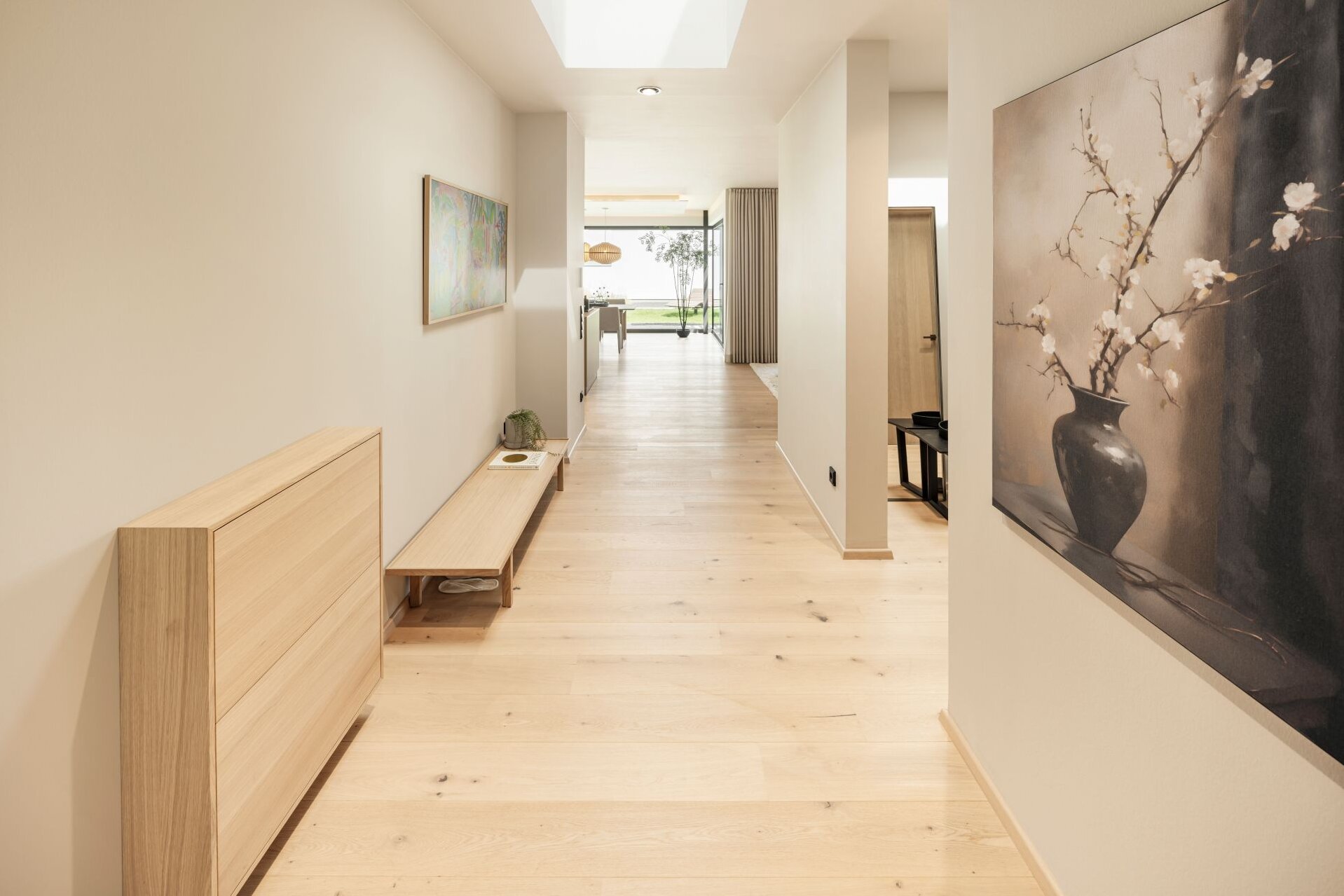 Langer Flur im FingerHaus Musterhaus NIVO in Frankenberg mit Holzboden, Sitzbank, Wandbildern und Oberlicht.