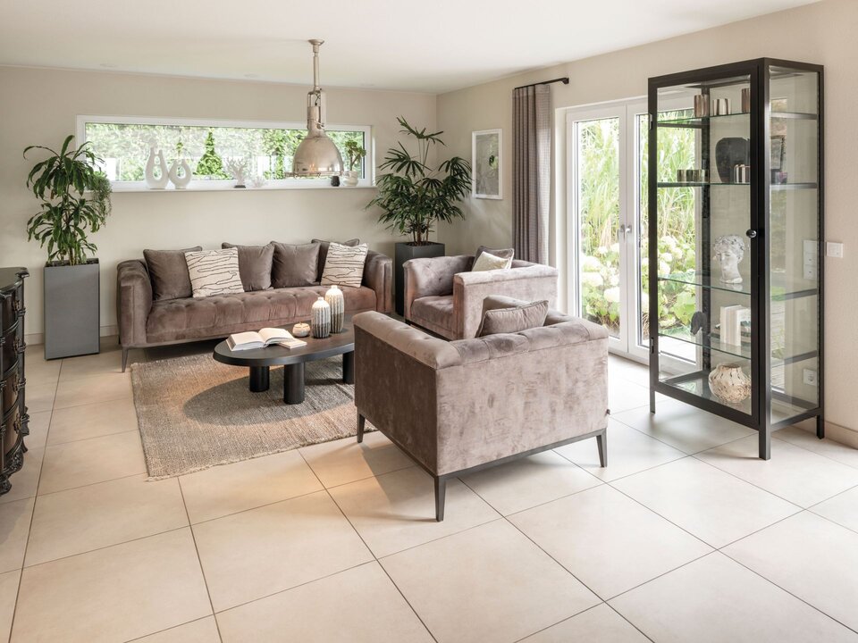 Wohnzimmer im FingerHaus Musterhaus NEO in Wuppertal mit eleganten grauen Sofas, Glastürenschrank und moderner Dekoration. Große Fensterfronten sorgen für viel Licht und einen offenen Blick in den Garten.