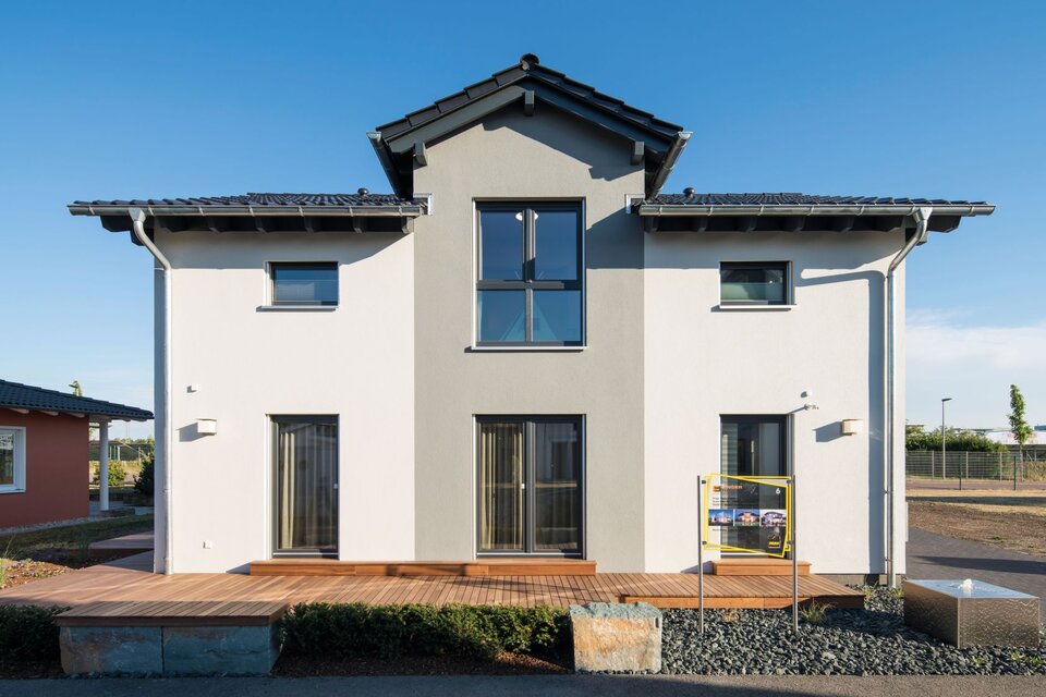 Frontansicht des Musterhauses UNO 2.0 in Leipzig mit moderner Architektur, großem Balkonfenster und Holzterrasse.