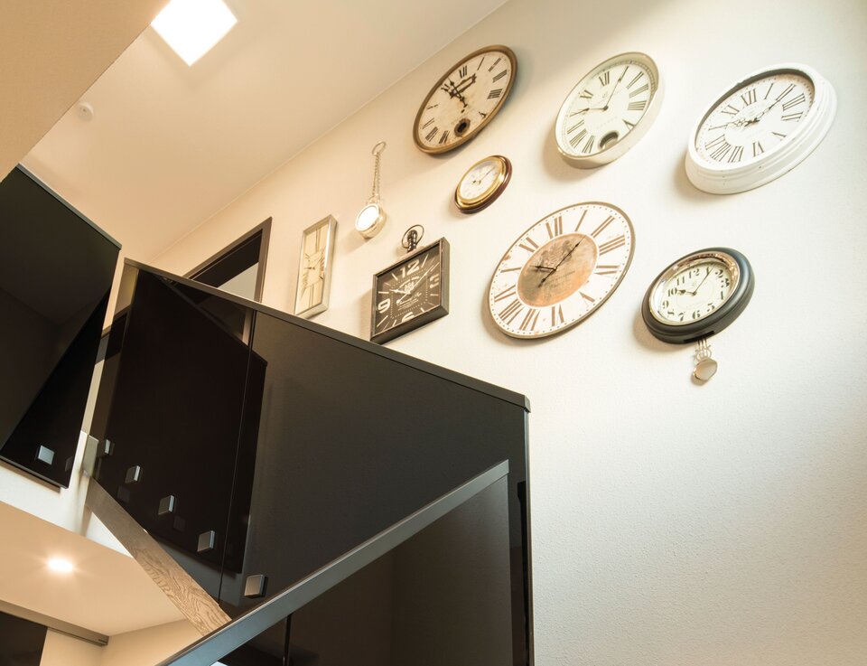 Moderne Holztreppe im Musterhaus ALTERO in Gießen mit dekorativer Uhrenwand und stilvollem schwarzen Geländer.