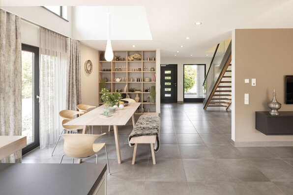 Essbereich im FingerHaus NEO 300 Musterhaus Hannover mit großem Holztisch, moderner Sitzbank, offenen Regalen und offener Verbindung zum Eingangsbereich mit Treppe.