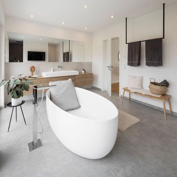 Modernes Badezimmer mit freistehender ovaler Badewanne, großem Spiegel und eleganter Holzeinrichtung.