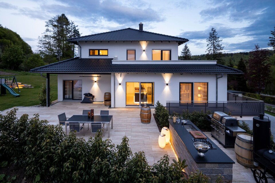 Großzügige Terrasse eines modernen FingerHaus mit Außenküche, Grillstation und stimmungsvoller Beleuchtung in der Abenddämmerung.