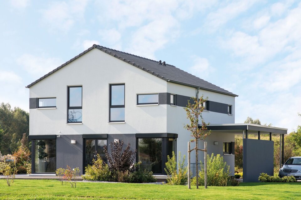 Modernes FingerHaus MEDLEY 300 B im Musterhaus Berlin/Werder mit klarer Fassadengestaltung, großem Carport und gepflegtem Garten bei Tageslicht.