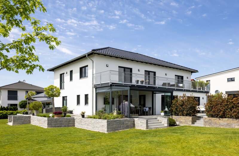 Modernes Zweifamilienhaus von FingerHaus mit Balkon, überdachter Terrasse und weitläufigem Garten an einem sonnigen Tag.