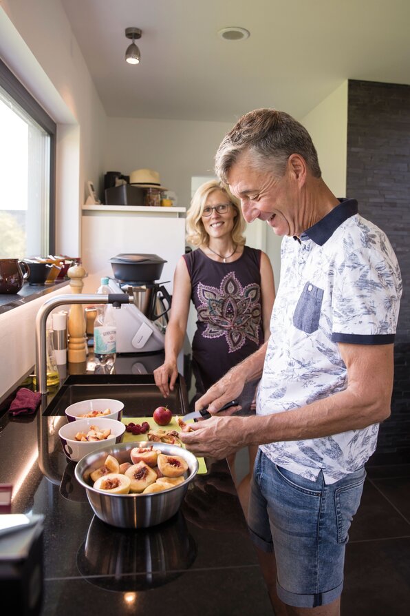 Zwei Personen bereiten in einer modernen Küche frisches Obst zu; Schalen und ein Schneidebrett liegen auf der Arbeitsfläche.
