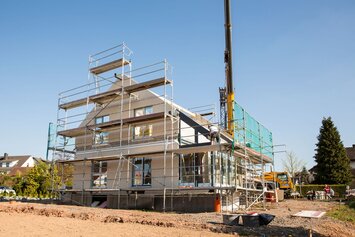 Montage eines Finger-Hauses mit Gerüst und Kran, Baustelle bei sonnigem Wetter.