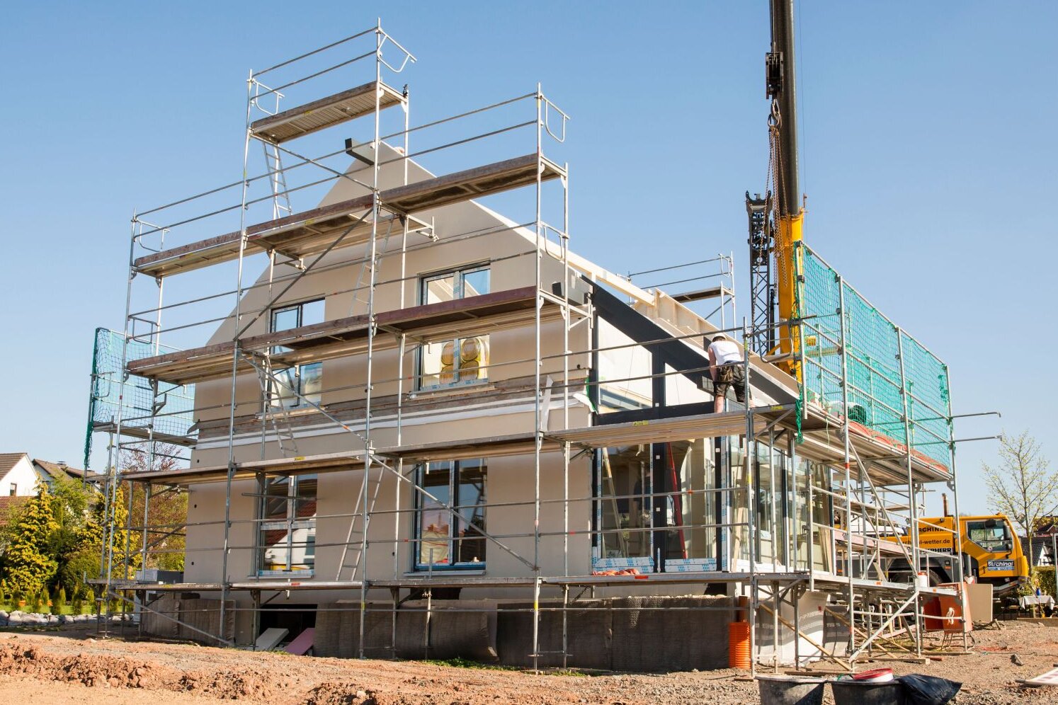 Montage eines Finger-Hauses mit Gerüst und Kran, Baustelle bei sonnigem Wetter.