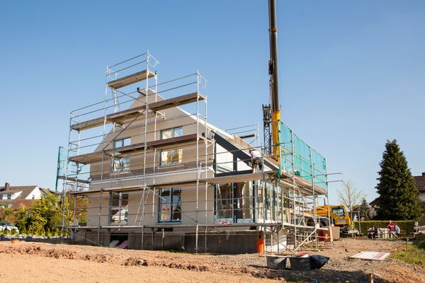 Montage eines Finger-Hauses mit Gerüst und Kran, Baustelle bei sonnigem Wetter.