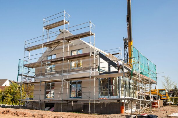 Montage eines Finger-Hauses mit Gerüst und Kran, Baustelle bei sonnigem Wetter.