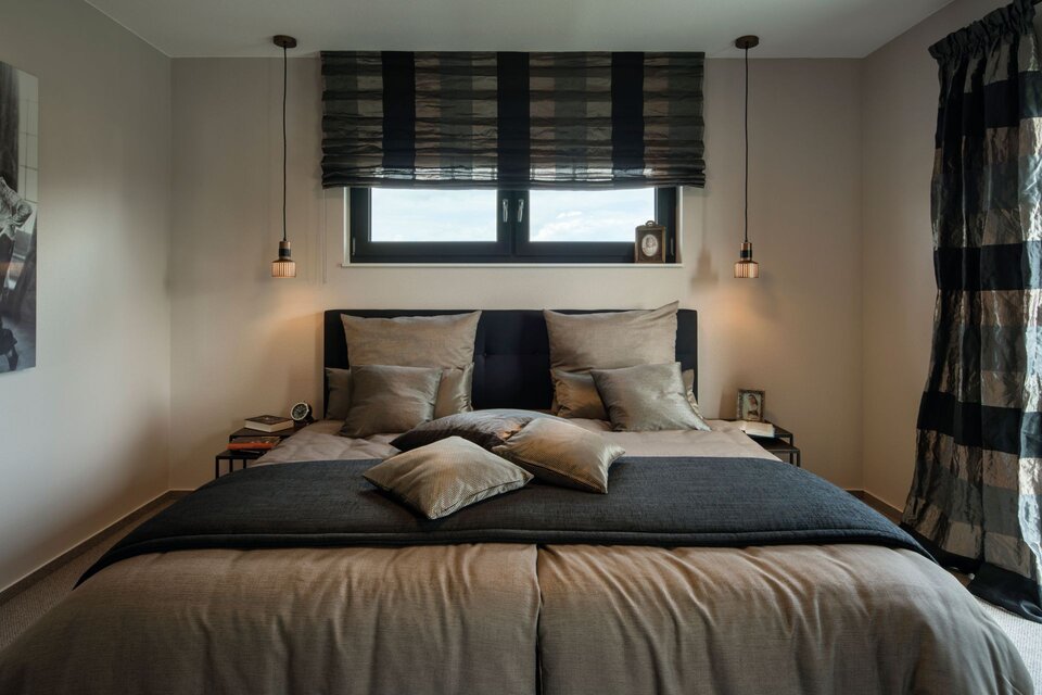 Schlafzimmer mit großem Bett, mehreren Kissen, zwei hängenden Lampen und einem Fenster mit Jalousie darüber