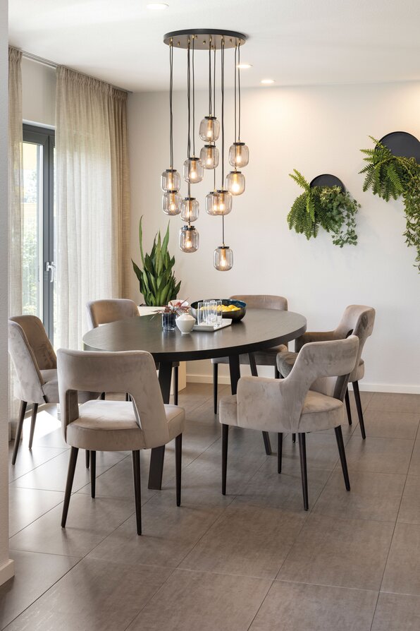 Essbereich im Musterhaus VIO Köln mit ovalem Esstisch, gepolsterten Stühlen und stilvoller Pendelleuchte.