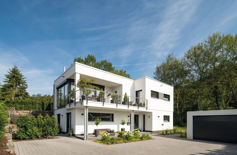 Modernes FingerHaus im Bauhausstil mit Flachdach, klaren Linien, großem Balkon, bodentiefen Fenstern und separater Garage, umgeben von Garten und Einfahrt.