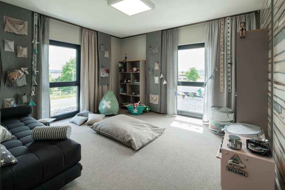 Kinderzimmer im Musterhaus ALTERO in Gießen mit kreativer Wandgestaltung, Spielbereich und viel Tageslicht durch große Fenster.