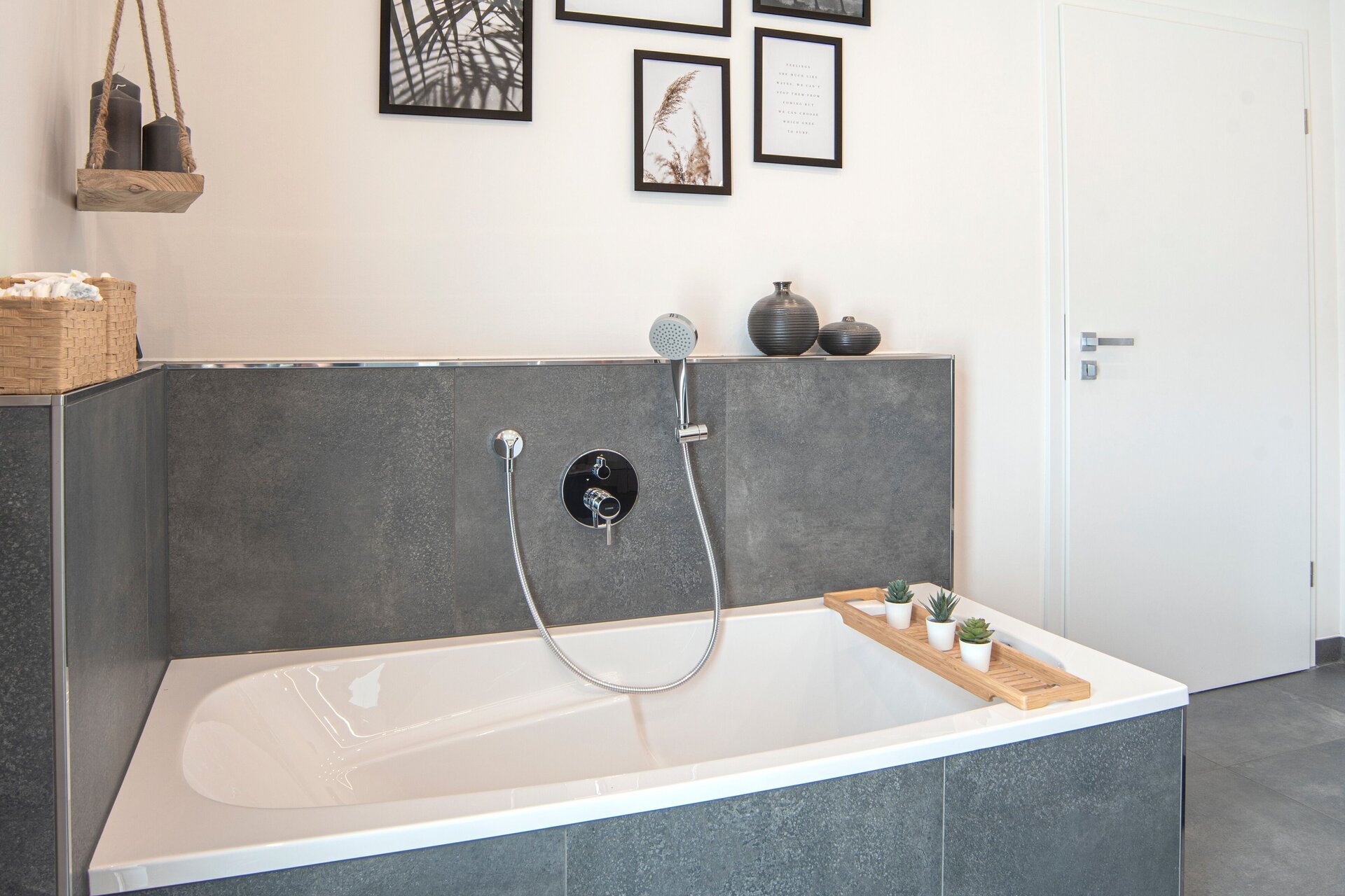 Modernes Badezimmer in einem FingerHaus NIVO 130 mit Badewanne, grauen Fliesen, Wanddekoration aus gerahmten Bildern und dekorativen Accessoires.