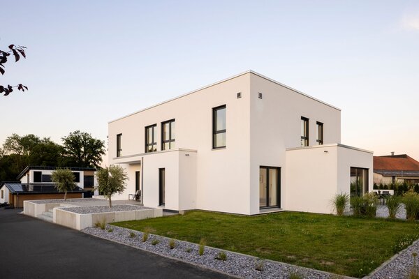Außenansicht eines modernen FingerHaus im Bauhaus-Stil bei Sonnenuntergang. Klare kubische Architektur, weiße Fassade und geradlinige Gartengestaltung mit Kiesflächen.