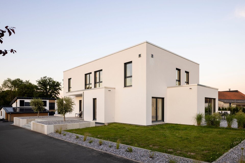 Außenansicht eines modernen FingerHaus im Bauhaus-Stil bei Sonnenuntergang. Klare kubische Architektur, weiße Fassade und geradlinige Gartengestaltung mit Kiesflächen.