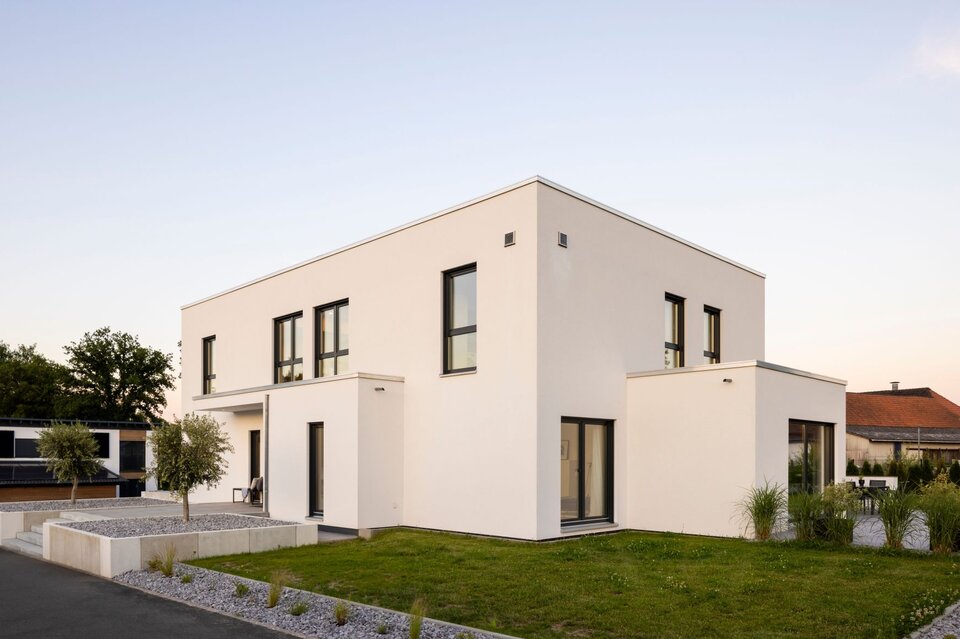 Außenansicht eines modernen FingerHaus im Bauhaus-Stil bei Sonnenuntergang. Klare kubische Architektur, weiße Fassade und geradlinige Gartengestaltung mit Kiesflächen.