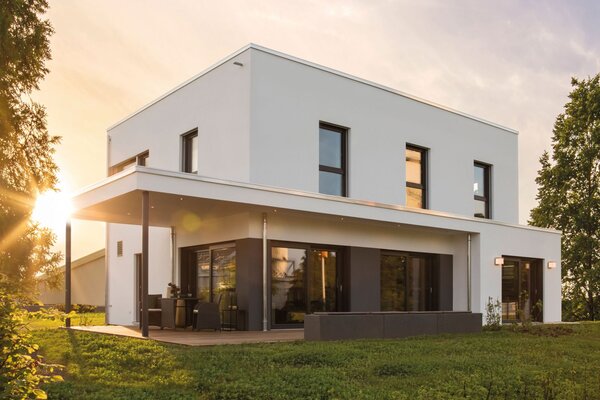 Modernes Flachdachhaus MAXIM mit überdachter Terrasse und klarer Fassadengestaltung im Abendlicht, Musterhaus Gießen.