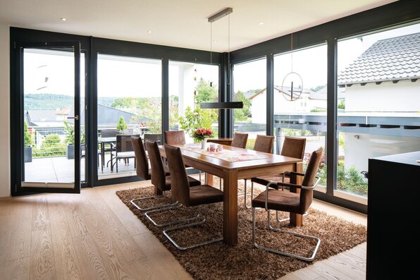Moderner Essbereich mit großem Holztisch und bodentiefen Fenstern in einem frei geplanten Finger-Haus.
