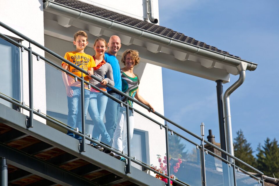 Familie steht auf dem Balkon ihres modernen FingerHaus-Hauses und genießt den sonnigen Ausblick.