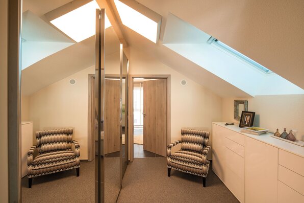 Ankleidezimmer im FingerHaus NEO Musterhaus Günzburg mit Dachschräge, Spiegelfronten und modernen Sitzmöbeln.