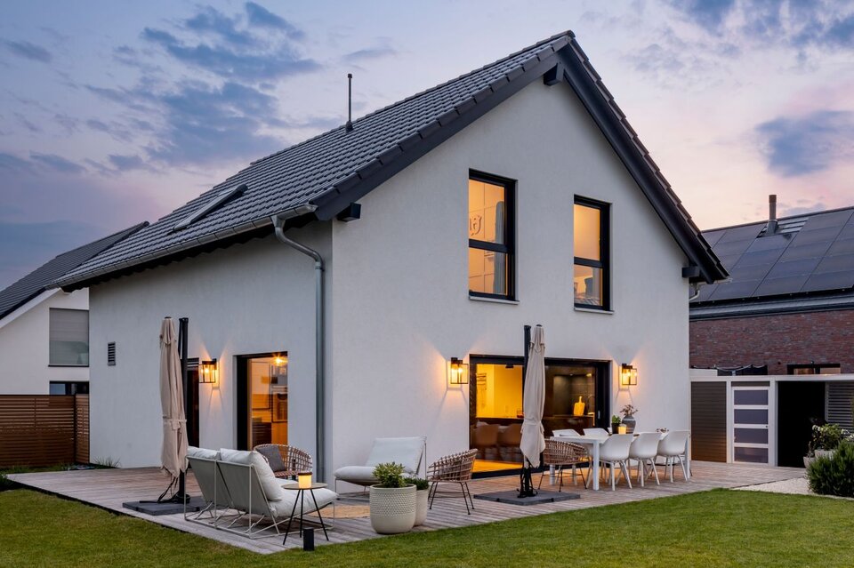 Frei geplantes FingerHaus bei Sonnenuntergang mit moderner Terrasse, stilvoller Beleuchtung und großem Garten.