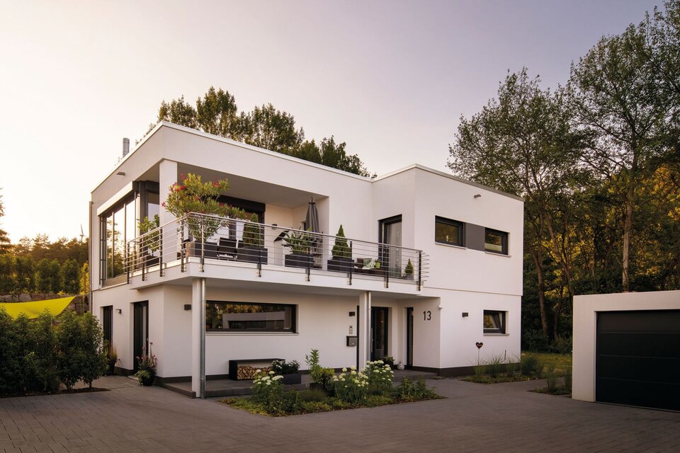 Modernes Flachdachhaus mit klaren Linien, großer Terrasse im Obergeschoss und gepflegtem Garten bei Sonnenuntergang.