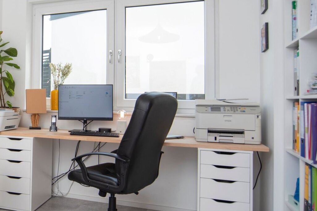 Ein modernes Homeoffice in einem FingerHaus-Haus mit großem Schreibtisch, Regalen und Computerarbeitsplatz. Ein kleines Kind steht spielend im Raum.