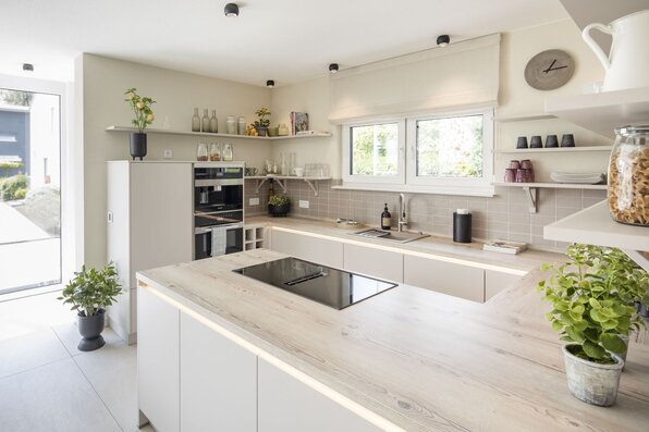 Helle, moderne Küche im MEDLEY Musterhaus Mannheim mit Kochinsel, offenen Regalen und stilvoller Ausstattung.