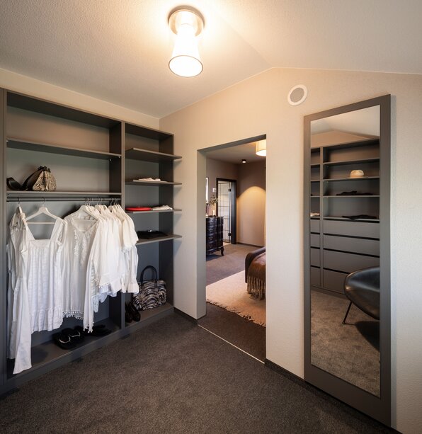 Ankleidezimmer im FingerHaus ARTIS 400 Musterhaus Schwarzwald mit offenen Regalen, Kleiderstangen, großem Wandspiegel und Verbindung zum Schlafzimmer.