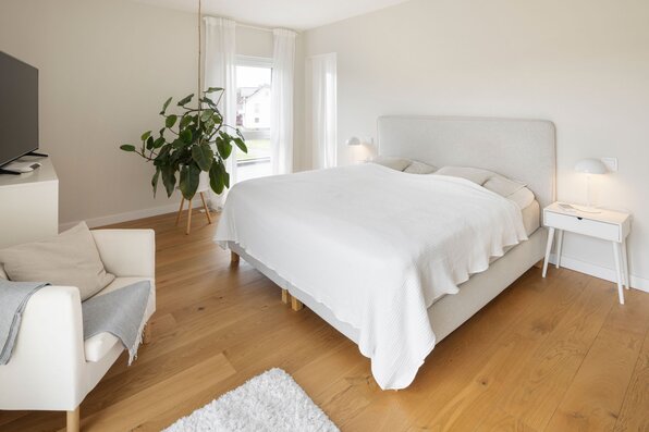 Helles Schlafzimmer mit modernem Doppelbett, weißen Möbeln und großem Fenster, das viel Tageslicht hereinlässt.