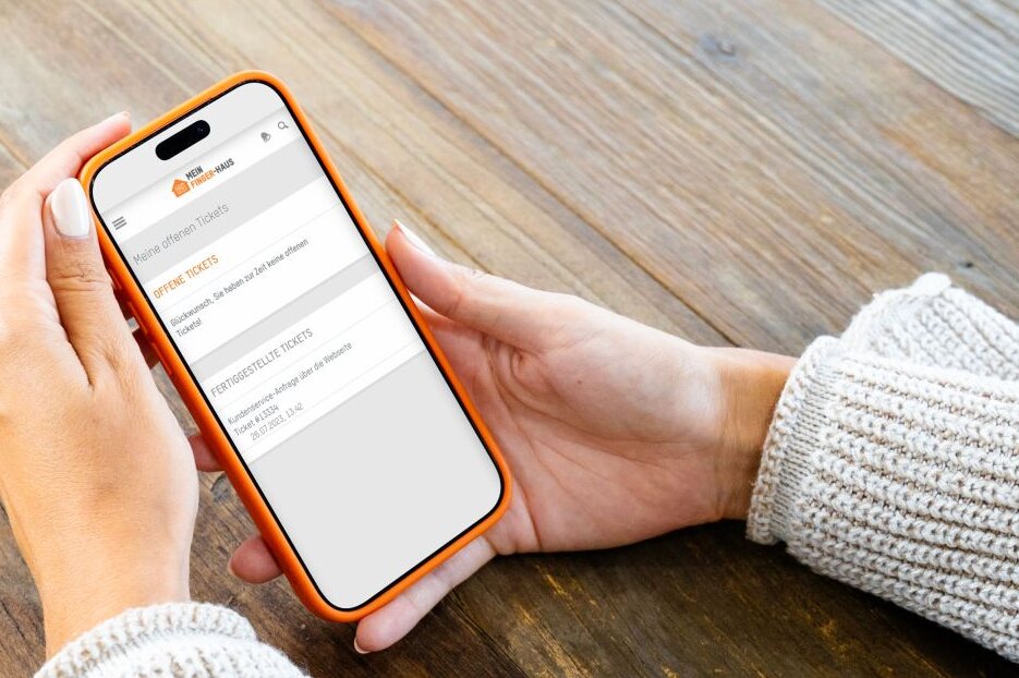 Person hält ein Smartphone mit dem FingerHaus Serviceportal in den Händen. Auf dem Display ist der Kundenservice für Hausbesitzer mit Service- und Kontaktoptionen zu sehen.