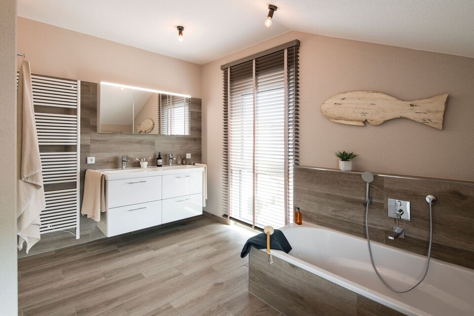 Modernes Badezimmer mit Badewanne, Holzoptik-Fliesen und stilvoller Waschtischanlage im Musterhaus UNO 2.0 Leipzig.