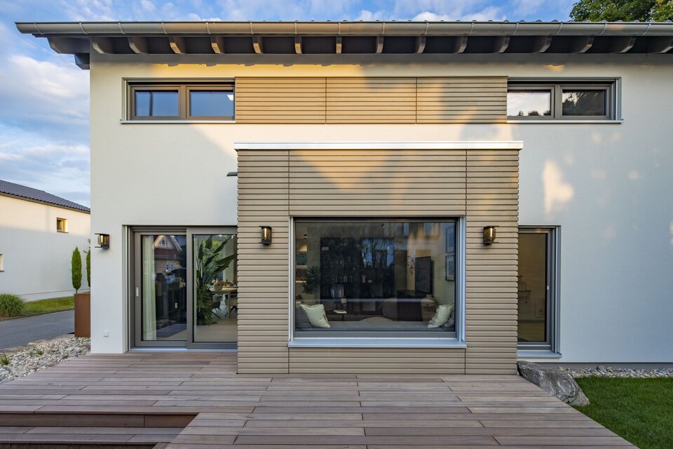 Seitliche Ansicht des FingerHaus MEDLEY Musterhauses in Mannheim mit moderner Holzfassade, großer Fensterfront und angrenzender Terrasse.