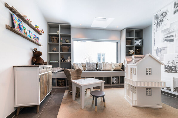 Helles und liebevoll eingerichtetes Spielzimmer mit Puppenhaus, Sitzbank und Regalen im Musterhaus MEDLEY 300 B in Poing.