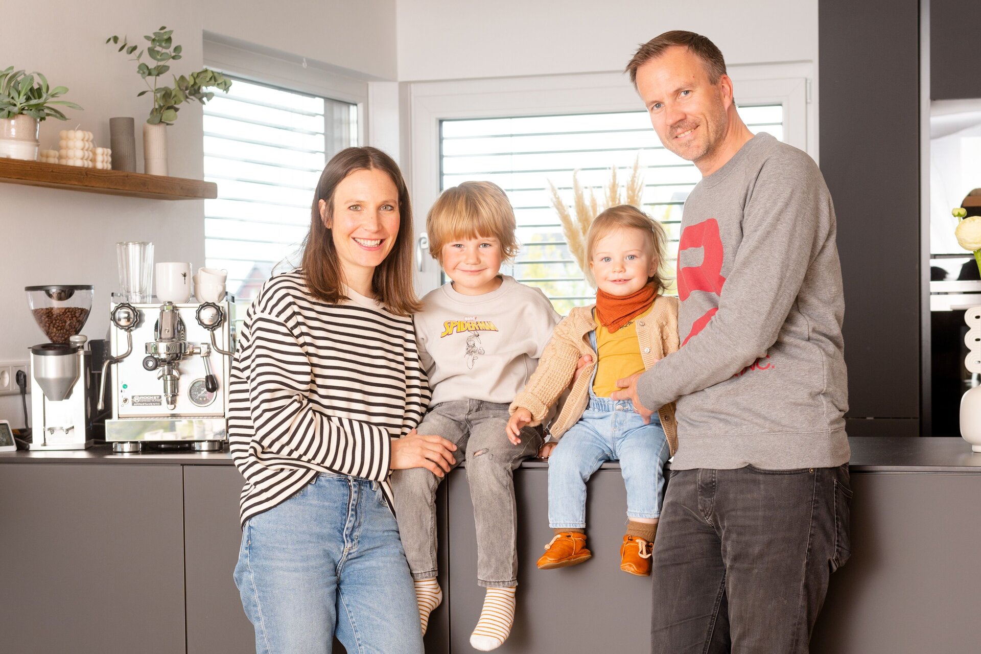 Familie im modernen, frei geplanten FingerHaus – gemütliches Beisammensein in der offenen Wohnküche mit viel Tageslicht.