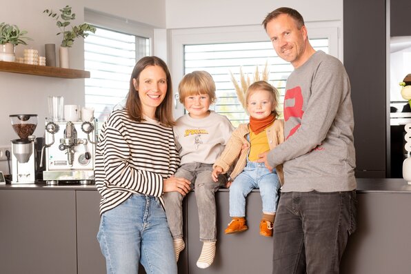 Familie im modernen, frei geplanten FingerHaus – gemütliches Beisammensein in der offenen Wohnküche mit viel Tageslicht.