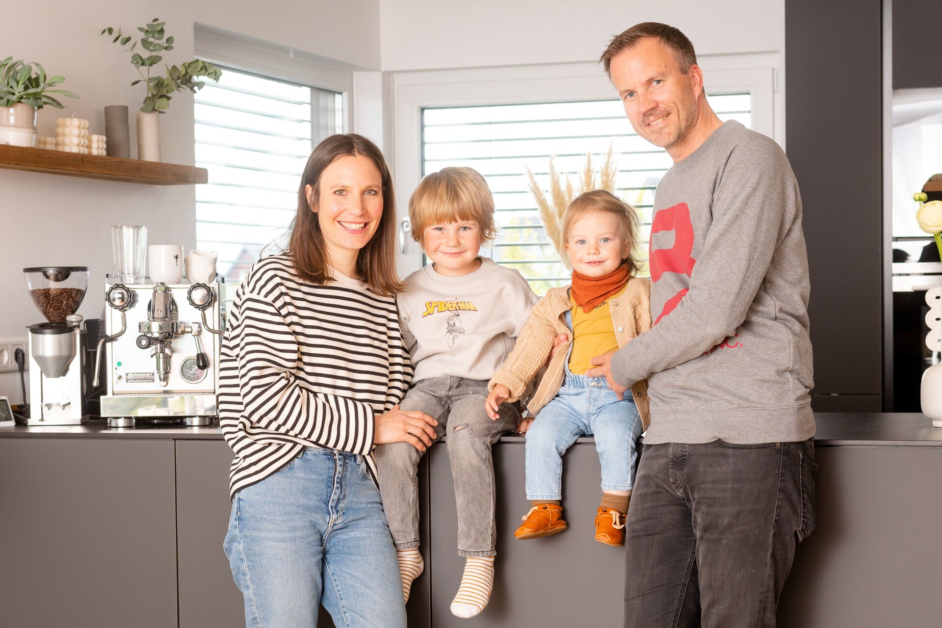 Familie im modernen, frei geplanten FingerHaus – gemütliches Beisammensein in der offenen Wohnküche mit viel Tageslicht.