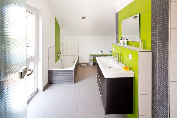 Modernes Badezimmer in einem frei geplanten Finger-Haus mit Badewanne, Doppelwaschbecken, großen Spiegeln und auffälligen grünen Wandfliesen als Akzent.