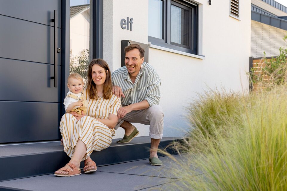 Frei geplantes FingerHaus mit modernem Eingangsbereich und Familie davor.