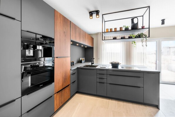 Moderne Küche im FingerHaus Musterhaus TALO in Babenhausen mit eleganten schwarzen Fronten, Holzakzenten und hochwertigen Elektrogeräten. Offenes Design mit Kochinsel, Hängeregal und viel Tageslicht durch große Fenster.
