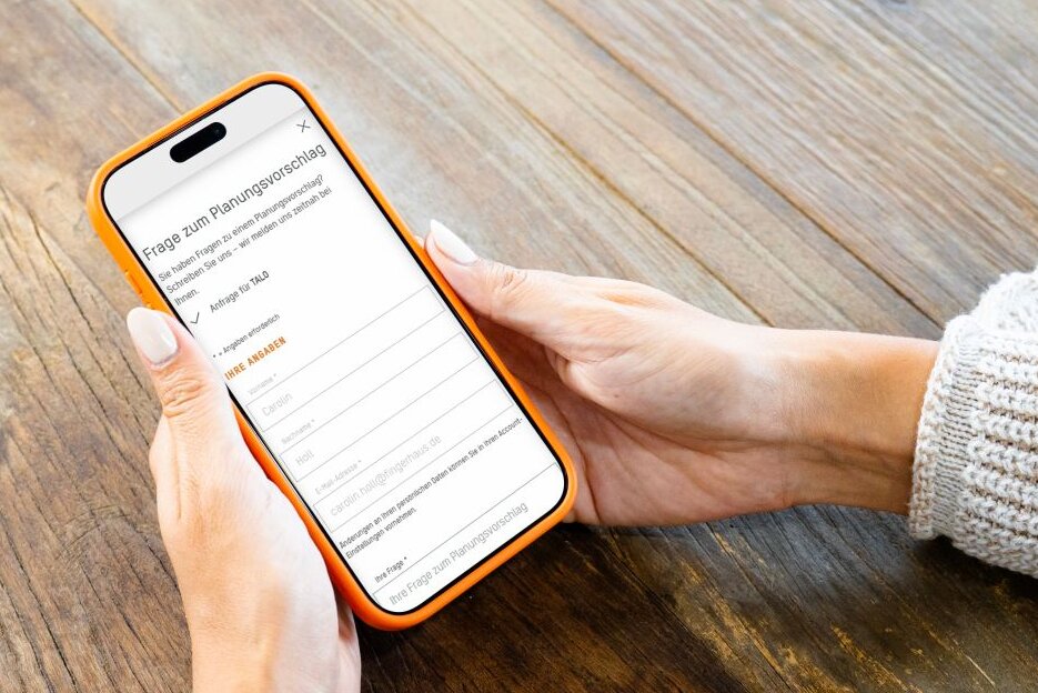 Person hält ein Smartphone mit dem FingerHaus+-Account in den Händen. Auf dem Display ist ein Formular zur Anfrage von Ausstattungsoptionen für mehr Komfort im geplanten Haus zu sehen.