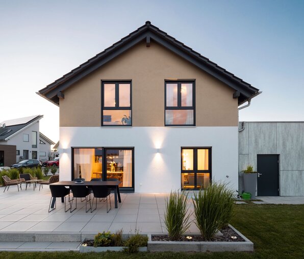 Finger-Haus NEO 211 mit Terrasse und beleuchtetem Wohnbereich in der Dämmerung.