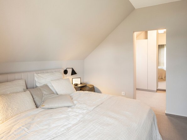 Gemütliches Schlafzimmer im Dachgeschoss des Musterhauses JUNO 300 in Mülheim-Kärlich mit hellem Bett und Zugang zur Ankleide.