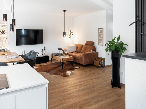Wohnzimmer des Kundenhauses NIVO 80 mit Ledersofa, Couchtisch, Fernseher und offenem Übergang zum Essbereich.