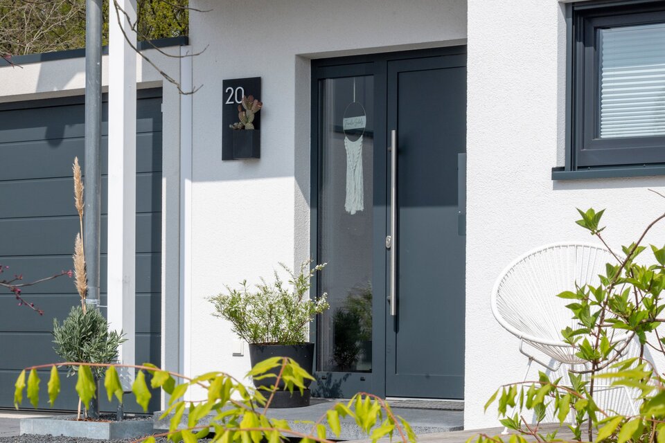Moderner Eingangsbereich eines frei geplanten FingerHaus mit grauer Haustür, überdachtem Zugang und stilvoller Außengestaltung.