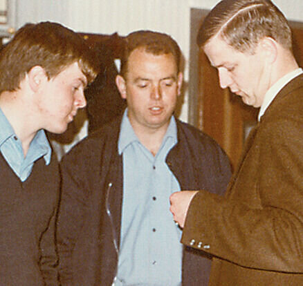 Hans-Adam Ochse und Willi Schäfer, ehemalige Geschäftsführer von FingerHaus, gemeinsam mit einer weiteren Person in einem Innenraum, drei Männer stehen dicht beieinander und betrachten ein Objekt in den Händen, historische Aufnahme.